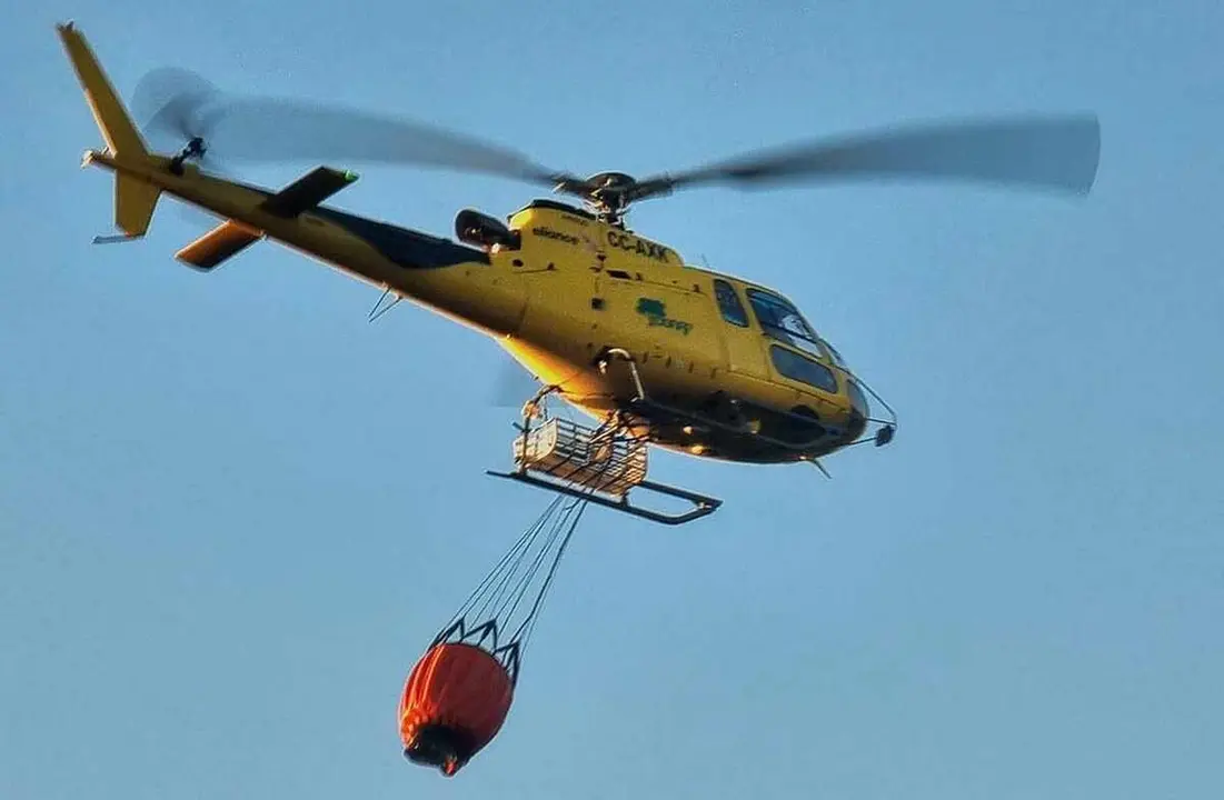 Un helicóptero con carga de agua se dispone a sofocar el incendio.