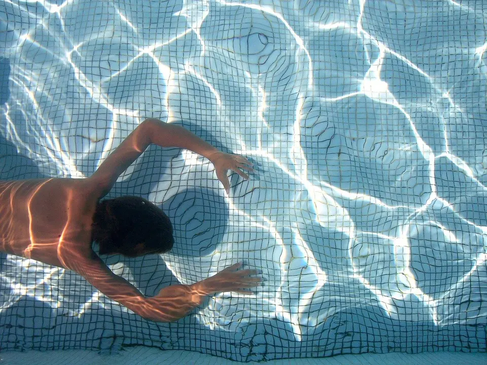 Un bañista avanza bajo el agua en una piscina pública.