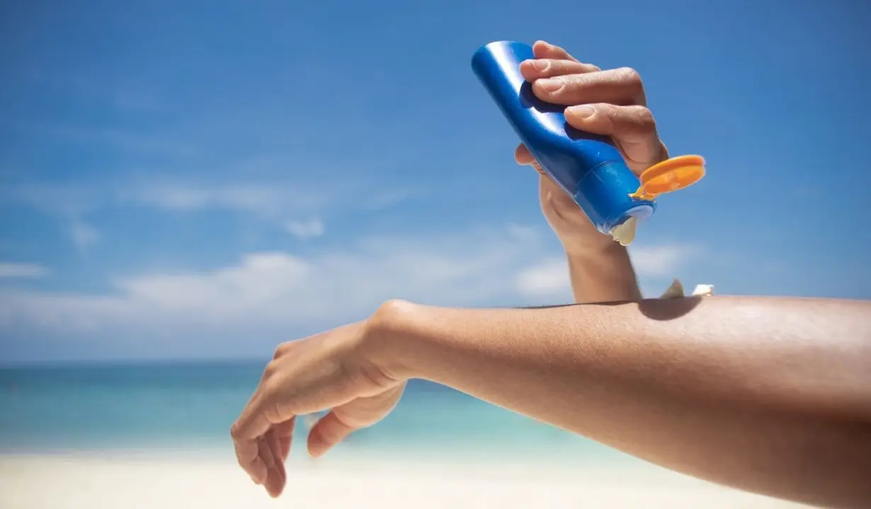 Woman applying sunscreen on her hands from a bottle on the beach with the sea in the background. SPF sunblock protection concept.selective focus