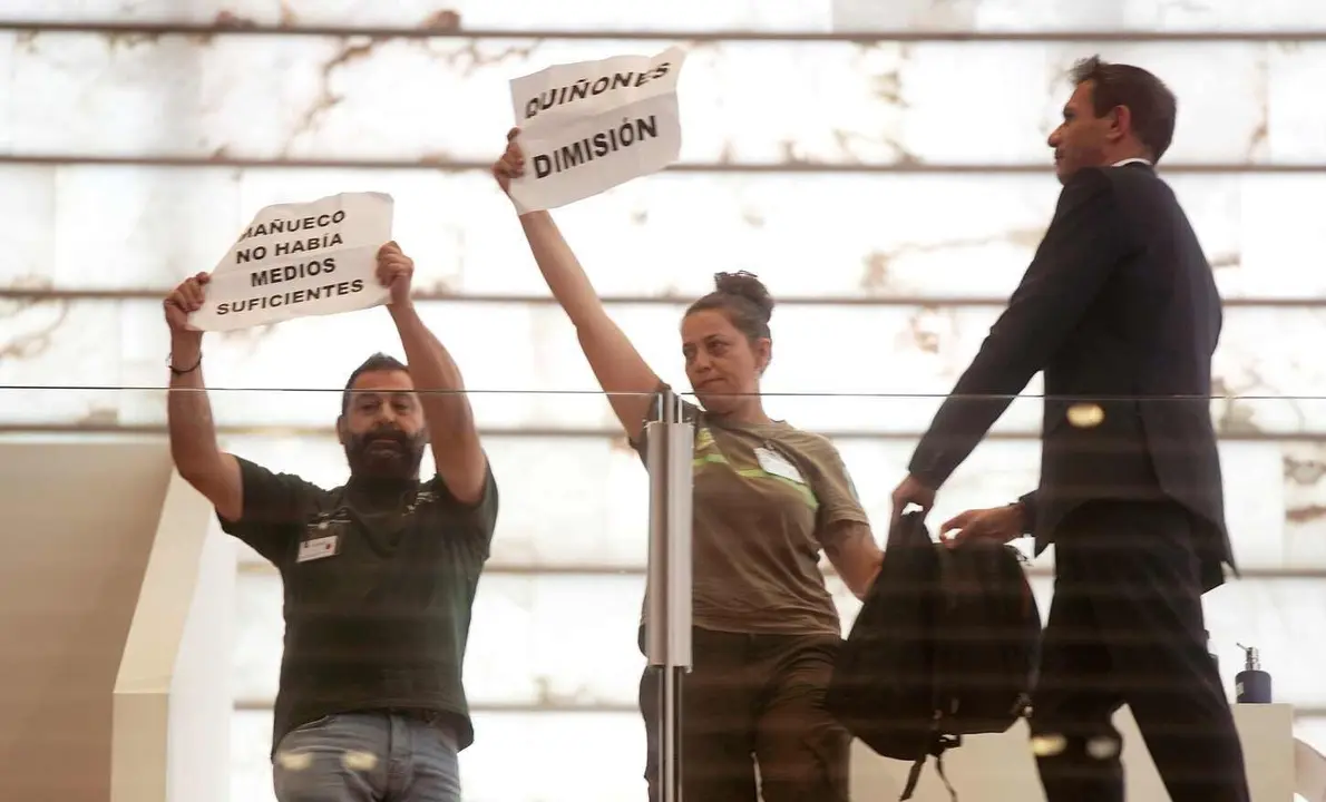 Dos bomberos forestales muestran pancartas durante el  Pleno extraordinario de las Cortes.
