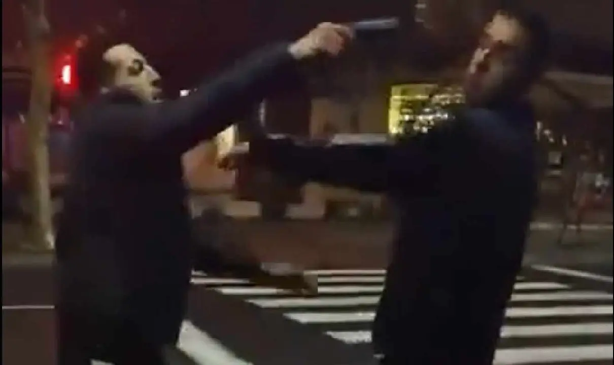 Momento en el que uno de los protagonistas del v&iacute;deo apunta al otro con una pistola.