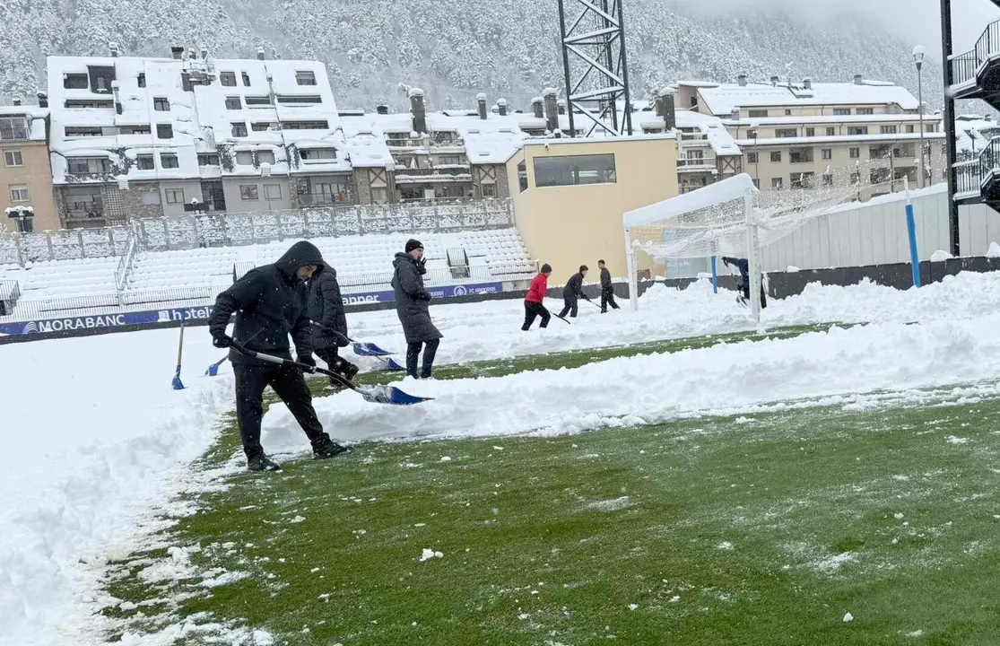 Empleados del Andorra trabajan en la retirada de la nieve del terreno de juego; la opci&oacute;n es intentar jugar pese a que se ha iniciado el tr&aacute;mite para su suspensi&oacute;n.
