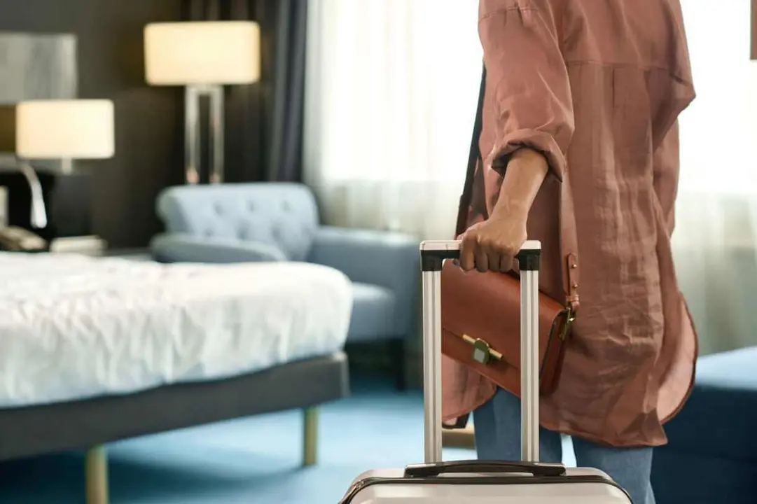 Close up of unrecognizable Black woman entering hotel room and holding suitcase upon travelling to resort copy space