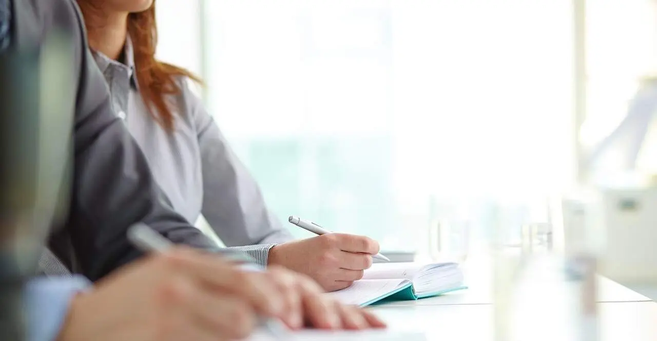 Hand of businesswoman with ballpoint over open notebook at convention