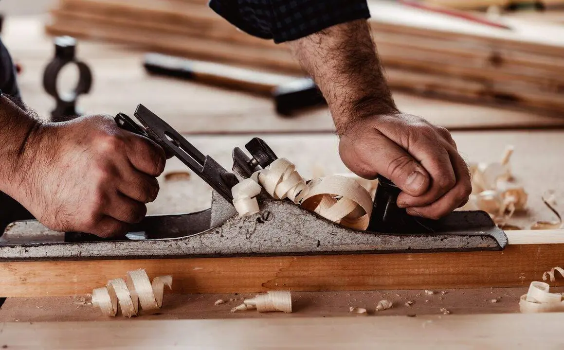 Carpenter's hands  planing a plank of wood with a hand plane close up