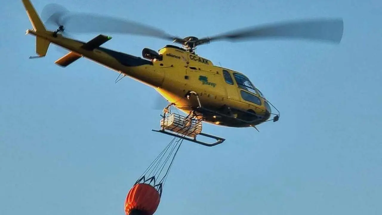 Un helicóptero con carga de agua se dispone a sofocar el incendio.