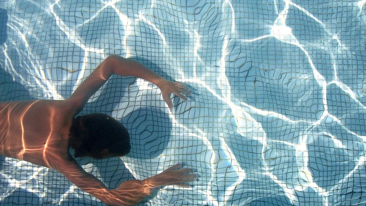 Un bañista avanza bajo el agua en una piscina pública.