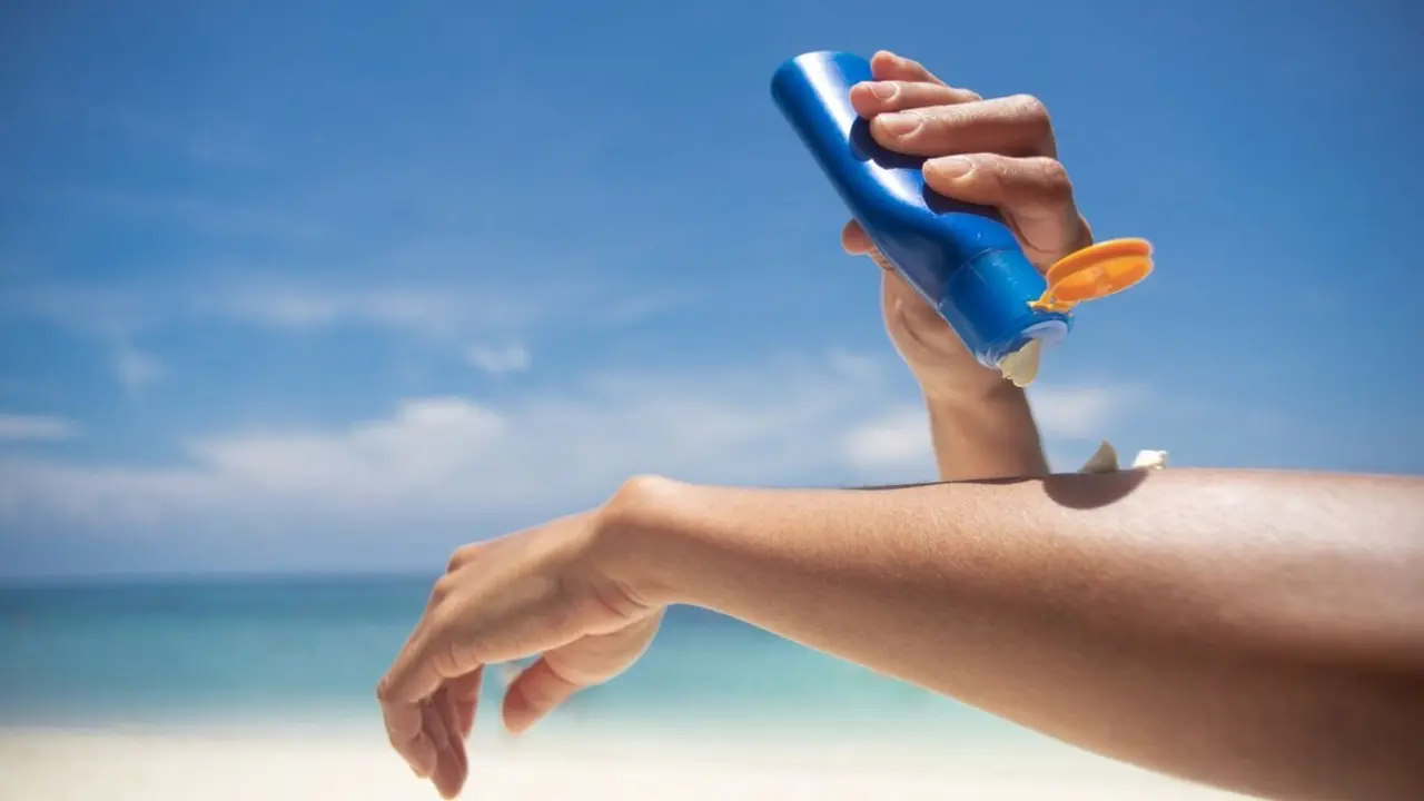 Woman applying sunscreen on her hands from a bottle on the beach with the sea in the background. SPF sunblock protection concept.selective focus