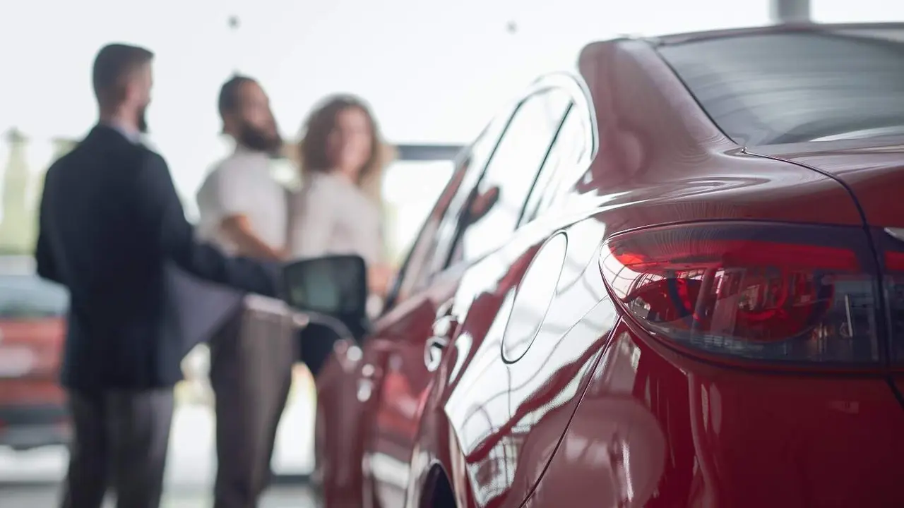 Back view of red car headlight close up. Clients standing near car dealer. Couple observing and seeking vehicle for purchase. Manager of car dealership showing automobiles.