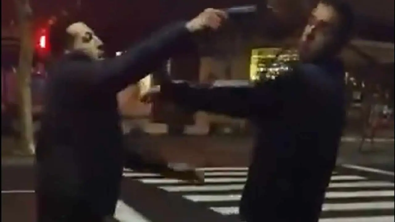 Momento en el que uno de los protagonistas del v&iacute;deo apunta al otro con una pistola.