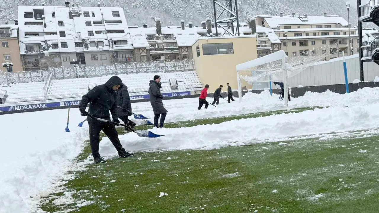 Empleados del Andorra trabajan en la retirada de la nieve del terreno de juego; la opci&oacute;n es intentar jugar pese a que se ha iniciado el tr&aacute;mite para su suspensi&oacute;n.