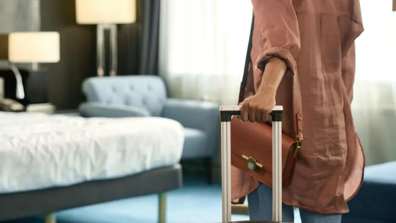 Close up of unrecognizable Black woman entering hotel room and holding suitcase upon travelling to resort copy space