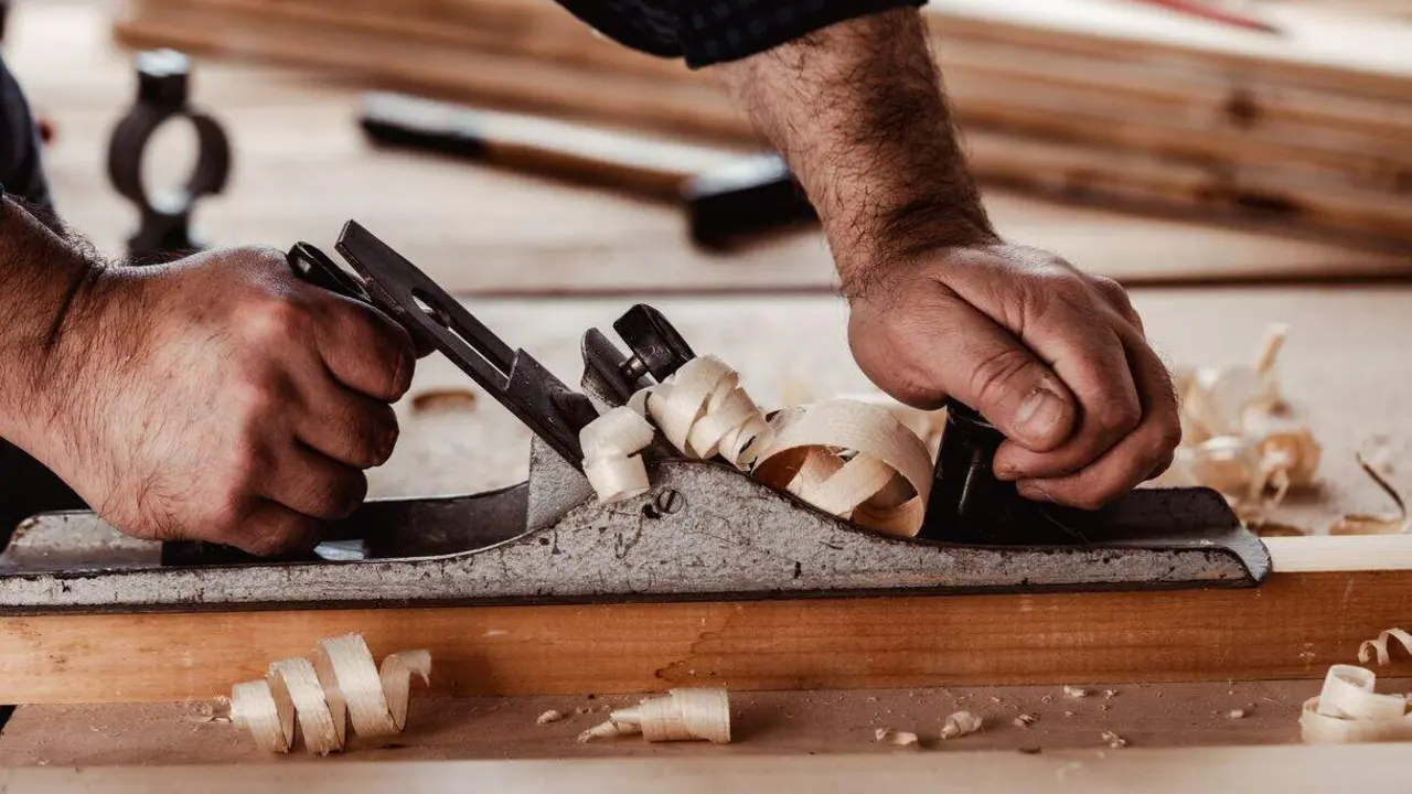 Carpenter's hands  planing a plank of wood with a hand plane close up