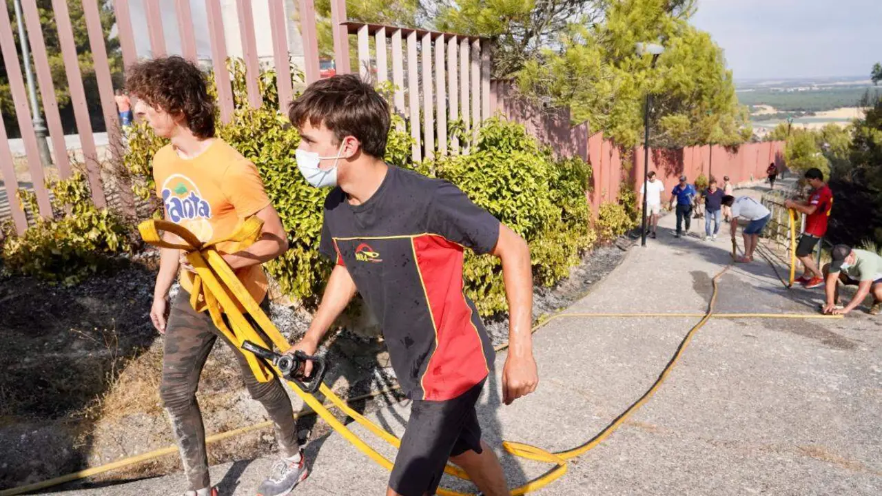 Un grupo de vecinos mueve mangueras para luchar frente al fuego.