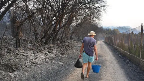 Un vecino intenta, con calderos de agua, sofocar los restos de las llamas. La imagen, publicada por El Bierzo Digital, ha sido realizada por Quinito.