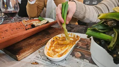 Un comensal moja el calçot en la salsa romesco durante el servicio en mesa.
